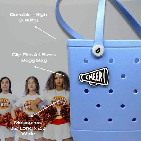 A BOGLETS black megaphone charm by Chatelet Manufacturing, compatible with Bogg Bags and sized 3.2 x 2.3, is shown on a tote in front of cheerleaders. Text highlights its durability and ideal size for cheer teams.