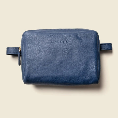 A blue leather Fanny Pack by CASUPO with a left-side zipper and CASUPO embossed on the front, photographed against a beige background.