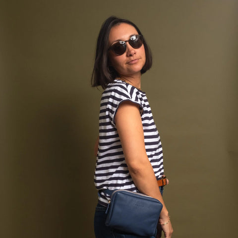 A woman in sunglasses and a black-and-white striped shirt poses against an olive green backdrop, confidently carrying the CASUPO Fanny Pack - Blue.