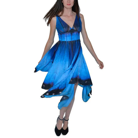 A woman models the Spiritex Blue Morpho Butterfly Dress, a sleeveless V-neck with a vibrant blue and black pattern and handkerchief hem, against a white background.