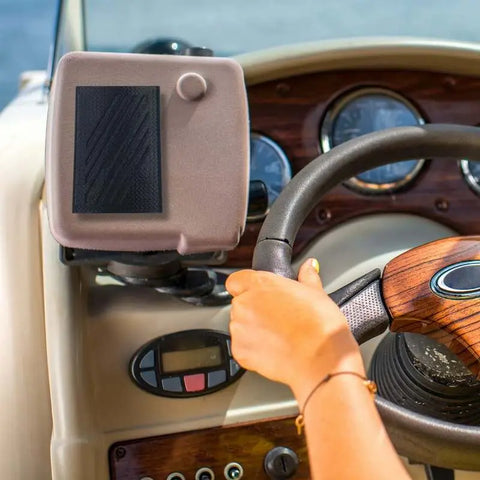 A person steers a boat with one hand on the wooden wheel. The dashboard and gauges are visible, along with a Chatelet Manufacturing FRESHe Boat Phone Holder (black), keeping a phone dry and secure on the water.
