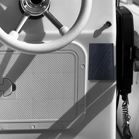 Close-up of a white boat dashboard with textured paneling, a mounted radio handset, and the Chatelet Manufacturing FRESHe Boat Phone Holder—black, easily mounts to any boat to keep your phone dry and secure while navigating.
