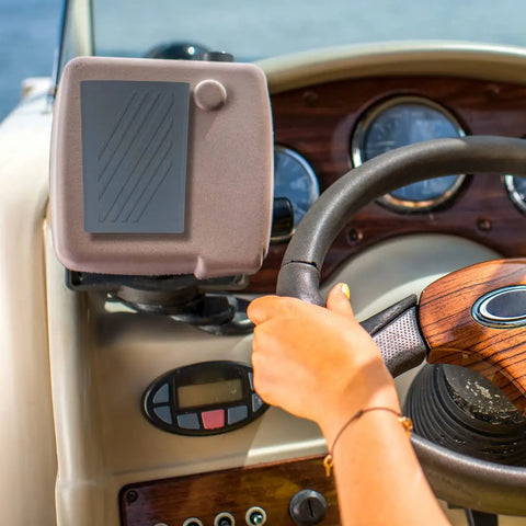 A person steers a boat, with navigation instruments and gauges on the dashboard, plus a Chatelet Manufacturing Boat Phone Holder—weatherproof, gray, made in the USA—to keep any phone dry and safe on the water.