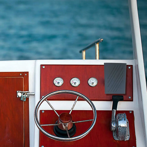 A Chatelet Manufacturing Boat Phone Holder, made in the USA and fitting any phone, is mounted by a durable steering wheel and control panel with gauges and levers—keeping your device dry and secure against the blue water backdrop.