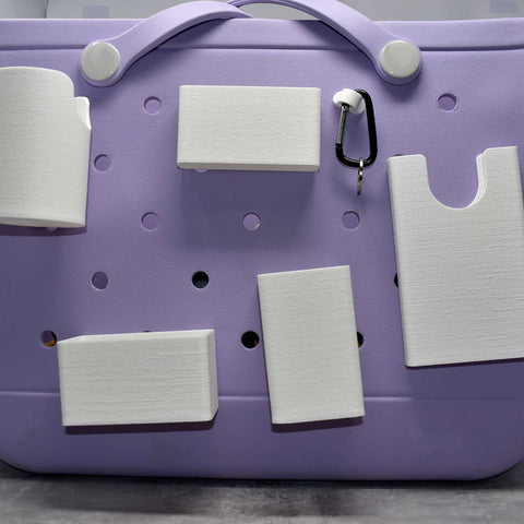 A Chatelet Manufacturing BAGLETS Ultimate Bundle in white, with key and wallet holders, phone case holder, bottle holder, sunglasses holder, and carabiner key holder attached to a lavender Bogg Bag with circular holes, shown on a gray surface.