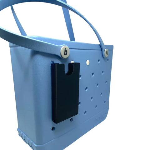 A light blue rubber tote bag with two handles features the Chatelet Manufacturing BOGLETS Phone Holder Charm Accessory, compatible with Bogg Bags, attached to its side. The background is plain white.