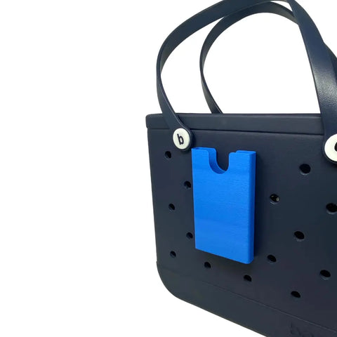 The BOGLETS Phone Holder Charm Accessory by Chatelet Manufacturing keeps your phone handy in your tote bag. Compatible with Bogg Bags, this USA-made holder features a bright blue pocket and fits totes with perforated holes and black handles.