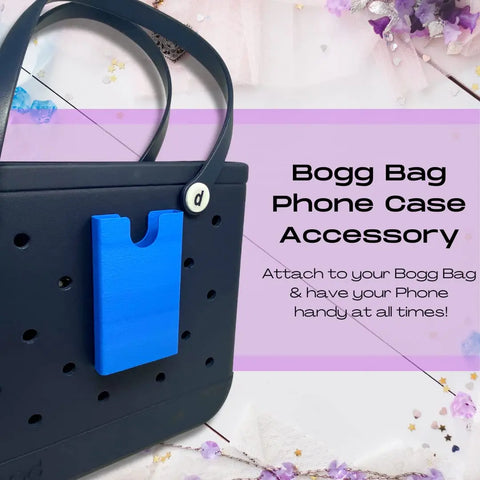 A blue BOGLETS Phone Holder Charm Accessory by Chatelet Manufacturing is attached to a black Bogg Bag tote, keeping your phone handy. Text reads: “Attach to your Bogg Bag & have your phone handy at all times!” Floral decor in background.