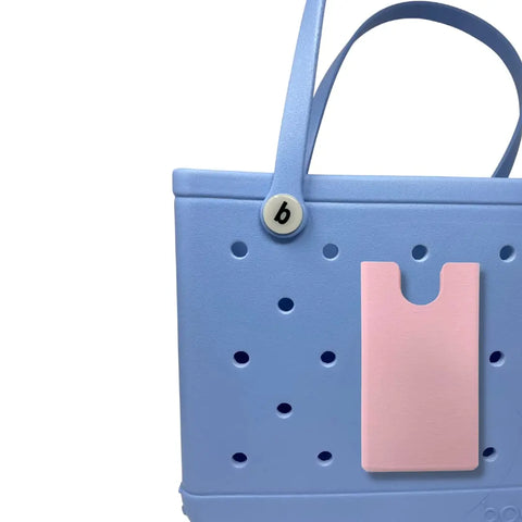 A light blue rubber beach tote with circular holes, featuring the Chatelet Manufacturing BOGLETS phone holder charm accessory (pink, rectangular) and a round b button near the handle, shown against a white background.