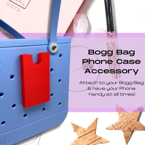 A blue rubber beach tote bag features a red BOGLETS Phone Holder Charm Accessory by Chatelet Manufacturing, keeping your phone handy with your Bogg Bag. Compatible with Bogg Bags and made in the USA. Pen and ribbon shown in background.