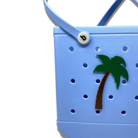 Add a fun touch to your bag with Chatelet Manufacturing’s BOGLETS Bogg Bag BEACH Charm accessories—decorative charms perfect for personalizing your tote. Shown: light blue bag with palm tree accent and round b button on white background.