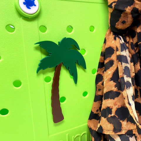 A green Crocs shoe with a palm tree-shaped charm and leopard print fabric, featuring BOGLETS by Chatelet Manufacturing—beach-themed decorative charms perfect for personalizing your Bogg Bag with unique accessories.