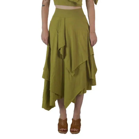 A person wears the Spiritex Tri Fab Layered Skirt in olive green, made from organic cotton, and brown open-toe wedge sandals, arms relaxed at their sides, shown from the waist down against a white background.