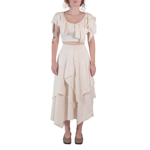 A person wears the Spiritex | Sustainable Apparel Boho Top in light cream with a matching tiered midi skirt, both made in the USA from organic cotton. The flowy, layered outfit is shown against a white background.