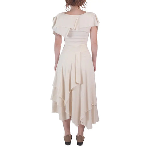 A woman with curly hair faces away against a white background, wearing an off-white Spiritex | Sustainable Apparel Boho Top and a matching organic cotton midi skirt with wedges.