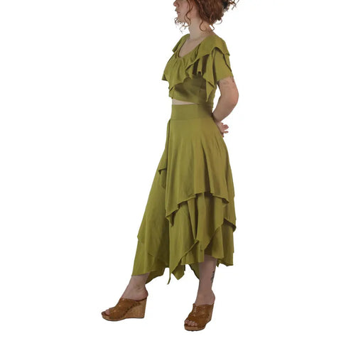 A woman in profile wears the Spiritex | Sustainable Apparel Boho Top in olive green organic cotton, paired with a matching asymmetrical skirt and brown wedge sandals, against a white background. Made in USA.