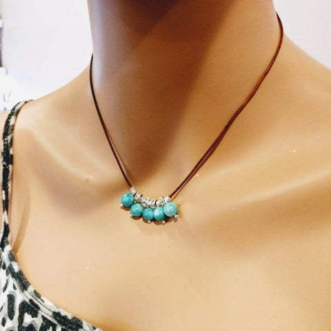 A mannequin displays Alexa Martha Designs Silver Green Blue Shell Bead Charm Leather Necklace, styled over a leopard print top.