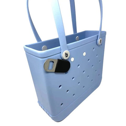 A light blue rectangular tote bag with perforated holes and two handles features the Chatelet Manufacturing BogLets Bottle Opener Charm Accessory for Bogg Bags, a black and silver stainless steel opener attached to the side with a round white button.