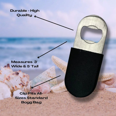 The BogLets Bottle Opener Charm Accessory by Chatelet Manufacturing, shown on a beach with seashells, features durable stainless steel, a 3-inch width, 5-inch height, and clips to any standard Bogg Bags tote for convenience.