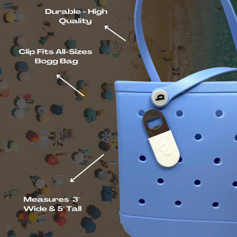 Close-up of a BOGLETS PREMIUM Bottle Opener Charm (White) by Chatelet Manufacturing, attached to a light blue tote. Clip fits all sizes of Bogg Bags, measures 3 wide & 5 tall, and is durable and high-quality. Beach scene in background.