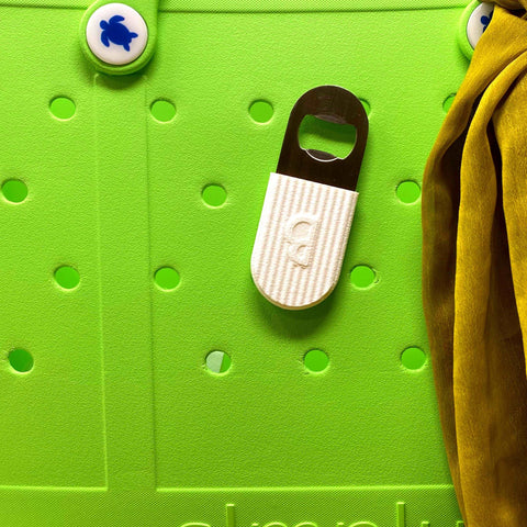 A bright green Bogg Bag features a Chatelet Manufacturing BOGLETS PREMIUM Bottle Opener (White) accessory charm attached, with blue button decorations and yellow fabric draped on the right side.