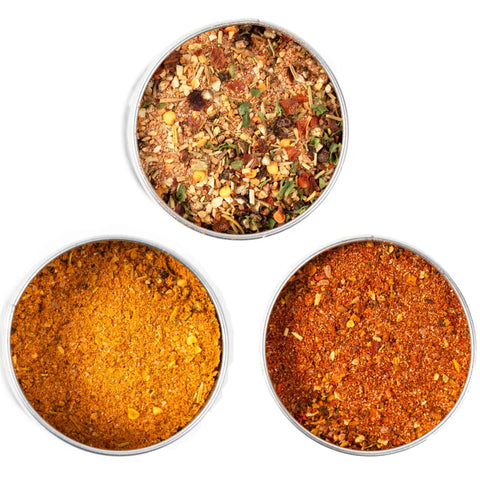 The Gustus Vitae Open Fire BBQ Collection - 3 Pack features three round containers, seen from above: a chunky mixed herb blend on top, and finely ground yellow and reddish-orange small batch BBQ rubs below.