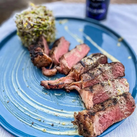 Sliced grilled steak, cooked medium-rare and seasoned with Gustus Vitae’s Open Fire BBQ Collection - 3 Pack, is served on a blue plate beside a cylindrical mound of sprouts or shredded veggies, drizzled lightly with sauce.