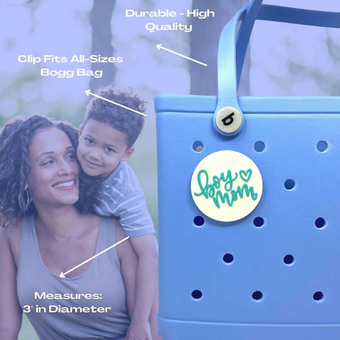 A smiling woman carries a boy outdoors. In front, a teal and white FRESHe BOGLETS Boy Mom Charm by Chatelet Manufacturing decorates a blue Bogg Bag. Text on the image highlights the charm’s features and dimensions.