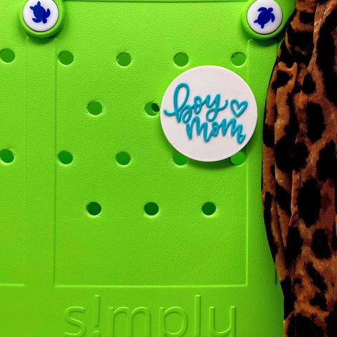 A FRESHe BOGLETS Boy Mom Charm (teal and white) from Chatelet Manufacturing decorates this bright green bag, paired with turtle-shaped charms and a leopard print fabric accent on the right side.