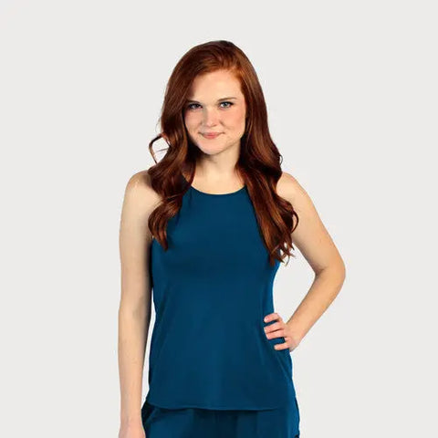 A woman with long, wavy red hair wears a sleeveless teal Lace Back Halter Top by Goodnighties, standing against a light gray background with one hand on her hip and a slight smile.