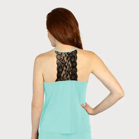 A woman with long red hair is seen from the back, wearing the Goodnighties Lace Back Halter Top in light blue with a black lace upper-back panel. Her right hand is on her hip, set against a plain light gray background.