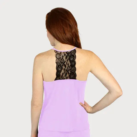 A woman with long red hair is seen from the back, wearing a sleeveless lavender Goodnighties Lace Back Halter Top with a black lace racerback. Her left hand is on her hip against a plain, light background.
