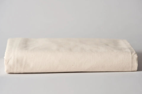 The American Blossom Linens Soft Cotton Baby Bedding Crib Sheet, in off-white, is neatly folded on a light gray surface. Its breathable fabric and cozy texture ensure comfortable sleep for your baby in any nursery.