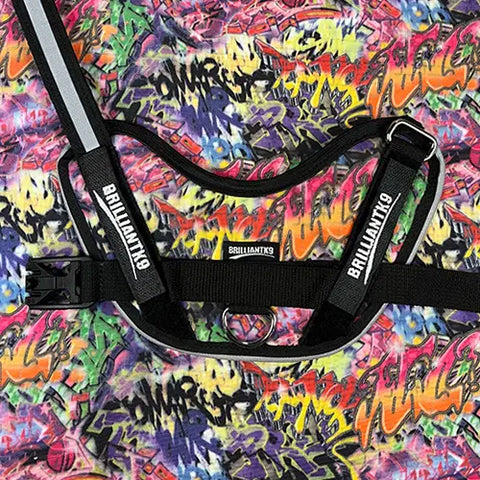 A close-up of a BrilliantK9 Ergonomic Dog Harness for XLarge Dogs 80 lbs and up, with an adjustable chest strap, set against a colorful graffiti-style background—ideal for extra-large breeds.