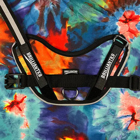 A colorful tie-dye fabric highlights the BrilliantK9 Ergonomic Dog Harness for little dogs 10lbs & under, featuring a metal ring, plastic buckle, and BrilliantK9 branding—perfect for toy breeds seeking comfort and style.