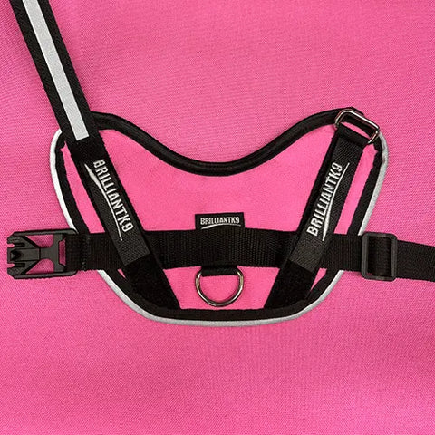 The BrilliantK9 Ergonomic Dog Harness for medium dogs (20–45 lbs) features a pink design with black trim, reflective stripe, plastic buckle, and metal D-ring, shown on a matching pink background.
