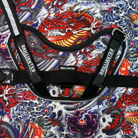 A close-up of the BrilliantK9 Medium Ergonomic No-Pull Dog Harness (20-45 lbs), Made in USA, featuring the BrilliantK9 logo on the straps, displayed on vibrant fabric with red dragons, koi fish, and swirling blue-purple patterns.