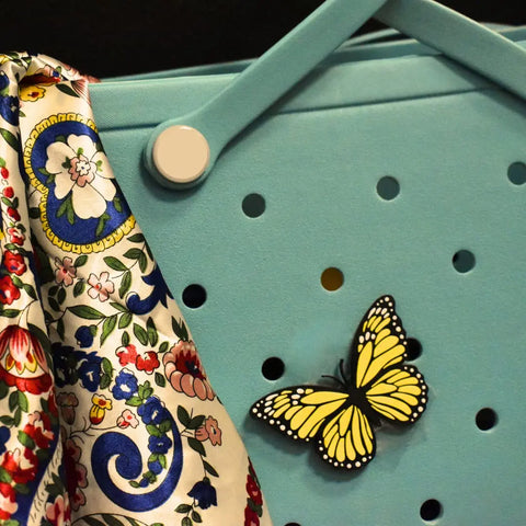 A FRESHe Baglets Bug Charm by Chatelet Manufacturing and a colorful floral-patterned scarf hang on a light blue pegboard with round holes and a large white peg.
