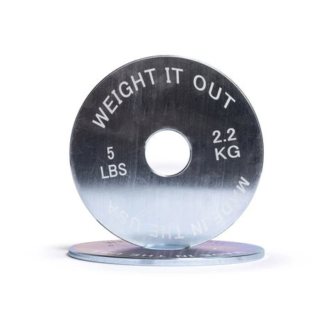 A silver Solid Steel Calibrated Weight Plate Pair from Weight It Out, labeled “5 LBS,” “2.2 KG,” and “MADE IN THE USA,” stands upright with another plate flat beneath it—ideal for Olympic bar workouts—against a white background.