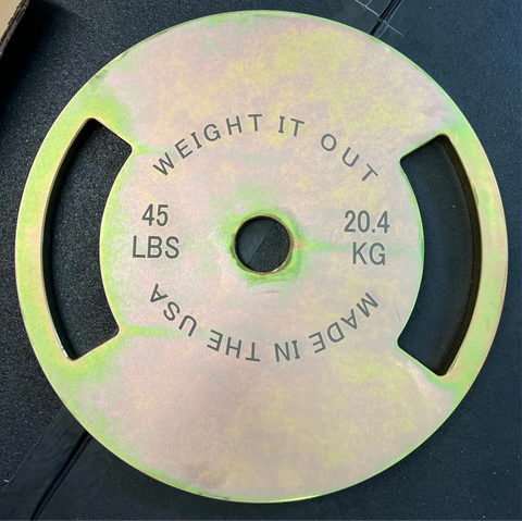 A round yellow-green Solid Steel Calibrated Weight Plate by Weight It Out (45 LBS/20.4 KG, MADE IN THE USA) with two grip handles rests on a dark surface.