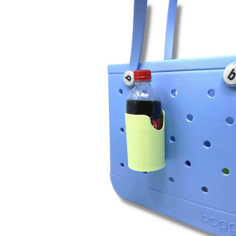 A light blue rubber tote with two handles and perforated design displays round lettered pins. It features the FRESHe BAGLETS Can Drink & Water Bottle Holder Charm Accessory by Chatelet Manufacturing, holding a soda bottle inside the bag.