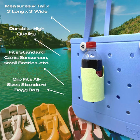 A light blue Rubber Tote Bag features the FRESHe BAGLETS Can Drink & Water Bottle Holder Charm by Chatelet Manufacturing, attached and holding a soda bottle. The durable holder fits all Bogg Bags, keeps drinks handy, and is made in the USA. Kayaks/water in background.