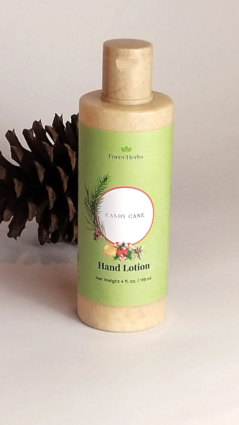 A bottle of Forev'Herbs Candy Cane Hand Lotion with a festive green label stands upright near a pinecone on a white surface, showcasing holiday greenery and promoting the natural peppermint ingredients.