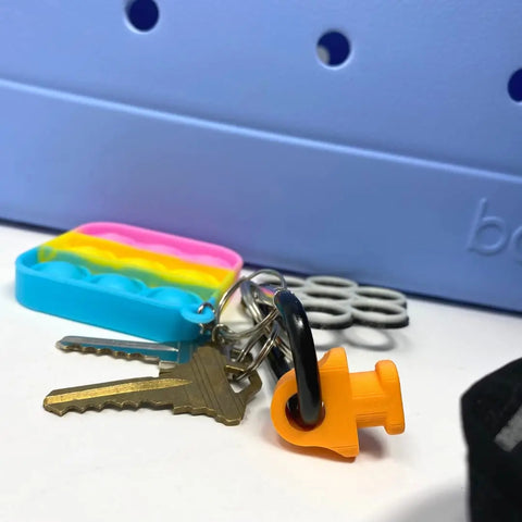 The BAGLETS Carabiner & Plug Keys Holder Charm by Chatelet Manufacturing secures keys or valuables and is perfect for rubber tote bags. Features a rainbow pop-it, silver keychain, and orange plug charm—Made in USA.