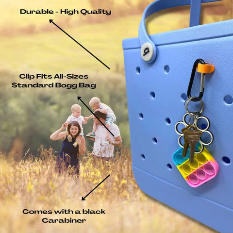 A BAGLETS Carabiner & Plug Keys Holder Charm by Chatelet Manufacturing secures keys and valuables on a blue rubber tote; a family of four stands in a field. Text highlights the accessory’s fit, durability, and secure key holding. Made in USA.