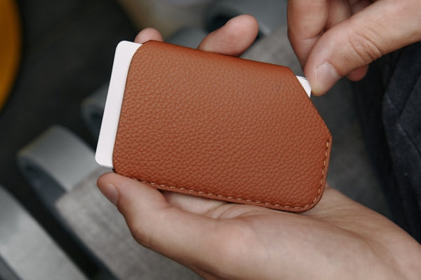 Brown leather cardholder held by a person with a blurred background