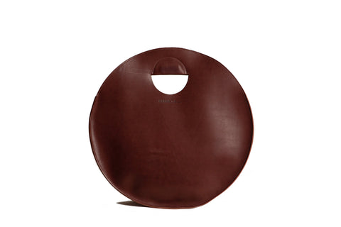 The Urban Southern Carrollton Circle Tote is a round, dark brown full-grain leather handbag with a built-in top handle, shown against a plain white background.