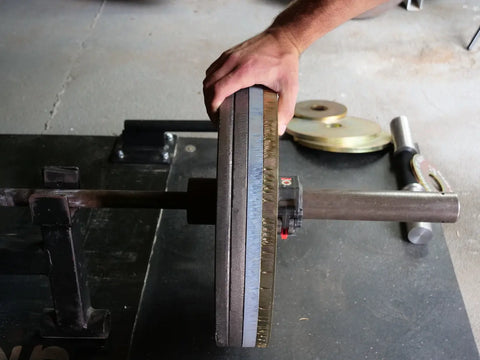 A hand loads a Weight It Out Cast Iron Machined Weight Plate Pair onto an Olympic bar in the gym, with additional plates and a bar resting on the concrete floor nearby.
