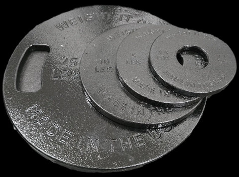 A stack of four black Weight It Out Cast Iron Weight Plate Sets (25 lb, 10 lb, 5 lb, 2.5 lb), each with engraved weight labels, is displayed against a black background to showcase their durability and size variety.