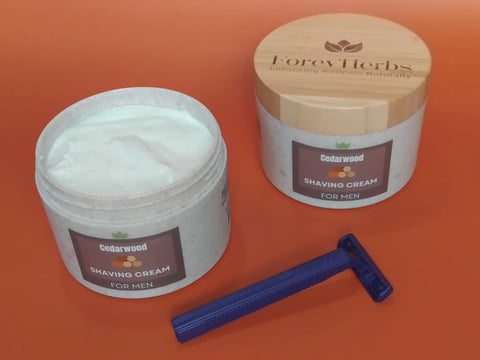 Open jar of Forev'Herbs Cedarwood Shaving Cream, a blue razor, and a closed jar with wooden lid on an orange surface; both jars are labeled Forev'Herbs.